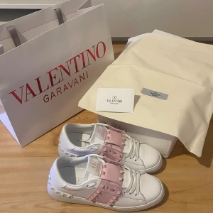 Valentino Rockstud sneakers vit/rosa - Snygga Valentino Rockstud sneakers i vitt skinn med ikoniska ljusrosa detaljer och nitar över vristen. Skorna använda fåtal gånger och är i bra skick men saknar en nit, se bild. Det syns dock inte så mycket när man väl har på sig de🥰