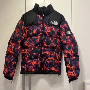 Supreme x North Face Lhotse pufferjacka XS - Säljer en fet The North Face 1990 Lhotse pufferjacka i XS med galet vulkaninspirerat mönster i svart, rött och orange. Jackan har hög krage, dragkedja och broderad logga på bröstet och ärmen. Perfekt för dig som vill sticka ut i vinterkylan. Det finns små vita prickar på ryggen och därför säljer jag den lite billigare men det är absolut inget som syns på långt hål. Om det finns någon fråga skriv gärna Mvh Mr.Vcloset