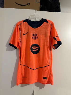 FC Barcelona third jersey, Pedri #8, Size: S/M - Säljer en FC Barcelona matchtröja från Nike med Pedri och nummer 8 på ryggen. Tröjan är orange med mörkblå detaljer, klubbmärke och sponsortryck på bröstet. Tillverkad i lätt och ventilerande material, perfekt för fotboll eller samling. New Condition, and player version  Size: S/M