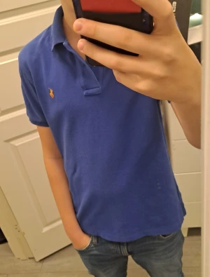 Blå slim fit piké från Polo Ralph Lauren xs - Snygg blå pikétröja från Polo Ralph Lauren med klassisk krage och korta ärmar. Slim fit-modell med orange broderad logga på bröstet. Materialet är mjuk bomull som känns skönt mot huden. Perfekt för dig som gillar stilren och sportig look. Passar xs hör av er vid frågor pris kan diskuteras.