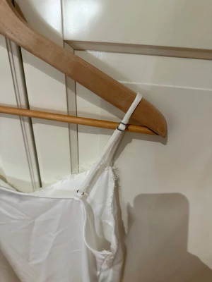 Vit linnetopp med spets från KappAhl - Supersöt och vit linnetopp från KappAhl med tunna justerbara axelband och vacker spetsdetalj längs v-ringad hals. 