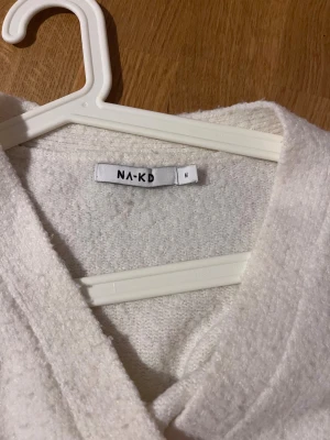 Vit omlottopp från NA-KD - Säljer en vit omlottopp från NA-KD i storlek M. Toppen har långa ärmar, v-ringning och knytband i midjan. Materialet är mjukt och lite fluffigt, vilket gör den extra mysig. Perfekt för dig som gillar stilrena och enkla plagg med en twist.