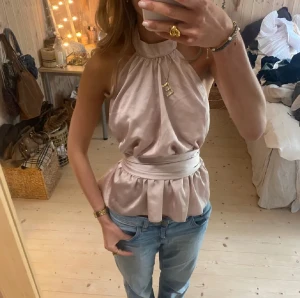 Champagnefärgad omlott blus med knyt - Säljer en champagnefärgad halterneck blus i glansigt satinmaterial. Toppen har hög hals, är ärmlös och har ett brett knytband i midjan som ger en snygg siluett. Passar Även S❣️