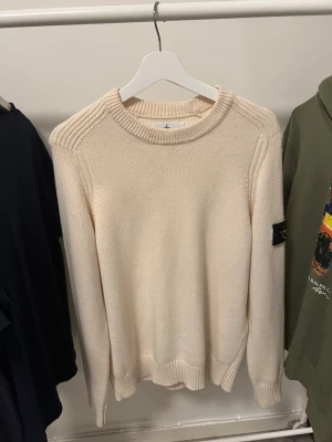 Beige stickad tröja Stone Island M - Snygg beige stickad tröja från Stone Island i storlek M. Tröjan har ribbade detaljer vid axlar, halsringning och muddar samt klassisk Stone Island patch på vänster ärm. Tröjan är nästintill helt ny använd några få tillfällen. Skicket är 9,5/10. Bra passform för M, kan nog passa S också. 