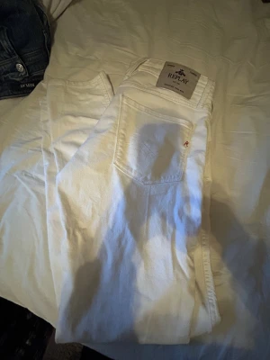 Vita Replay Anbass jeans slim fit - Säljer ett par fräscha vita Replay Anbass jeans med slim fit. Klassisk femficksmodell med snygga detaljer och metallknapp fram. Byxorna har en stilren look och passar perfekt till sneakers eller boots. Materialet är mjukt och bekvämt bomullstyg.