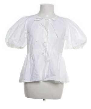 Vit blus med knyt från Nelly - Supersöt vit blus från Nelly med puffiga korta ärmar och flera knytningar framtill. Blusen har en lätt volang nertill och är tillverkad i ett tunt bomullstyg. Perfekt för en romantisk och trendig look. Passar mindre storlekar också den är lite trasig där man knyter rosetterna dom har spruckit lite!!! Men inge större problem