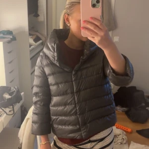 Grå dunjacka från Herno - Säljer en grå pufferjacka från Herno med bred krage och trekvartsärmar. Jackan har en snygg quiltad design och stängs med knappar framtill. Perfekt för dig som vill ha en stilren och cool look under kyliga dagar. Jackan är i storlek S/42IT. Finns smink fläckar på insidan av jackan uppe vid kragen. Ej provat tvätta bort de. 