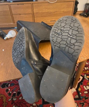 Svarta boots med nitar och spännen - Snygga svarta boots i skinn med rund tå, låg klack och platt sula. Dekorerade med silvriga nitar och två spännen på skaftet. Dragkedja på sidan för enkel på- och avtagning. Perfekt för dig som gillar en lite tuffare stil.