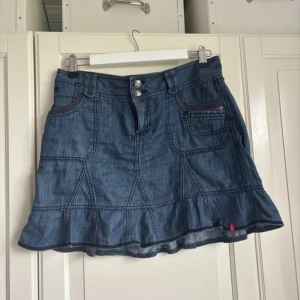 Blå jeanskjol med volangkant - Säljer en blå jeanskjol från Esprit med snygga detaljer som dubbla knappar framtill, flera fickor och volangkant längst ner. Kjolen har markerade sömmar och en cool, lite loose passform. Perfekt för dig som gillar denim 