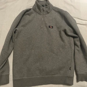 Grå half zip tröja från Dickies - Säljer en grå långärmad tröja från Dickies i storlek small. Tröjan har en hög krage med half zip och liten logga på bröstet. Tillverkad i mjuk bomullsmix, perfekt för chill dagar eller när du vill ha en enkel och clean look.