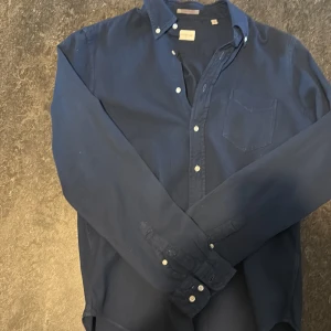 Blå GANT Rugger Indigo Waffle skjorta - Snygg blå skjorta från GANT Rugger, modell Indigo Waffle. Skjortan har en unik våfflad struktur i bomull, klassisk krage med knappar och bröstficka. Långärmad och med vita knappar framtill. Perfekt för dig som gillar stilrena och coola detaljer.