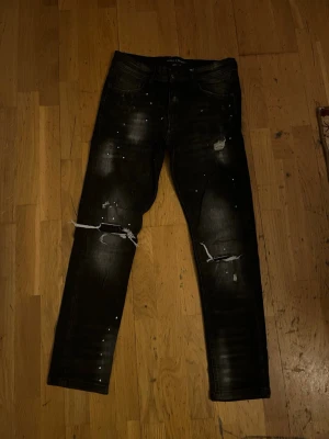 Svarta slitna jeans med hål - Säljer ett par svarta jeans med slitningar och hål på båda knäna. Jeansen har en slim fit.