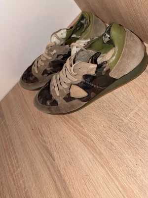 Philippe Model camo sneakers - Snygga sneakers från Philippe Model med camouflagemönster i grönt, brunt och beige. Skorna har mockadetaljer, gröna hälpartier och klassisk låg siluett. Perfekta för dig som vill sticka ut med en streetstyle-look.