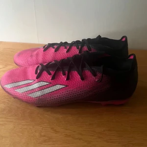 Adidas rosa fotbollsskor med dobbar - Säljer ett par snygga fotbollsskor från Adidas i rosa och svart med silvriga ränder på sidan. Skorna har klassisk snörning och en yttersula med fasta dobbar för bra grepp på planen. Ovandelen är i syntetmaterial och designen är slimmad för en snabb känsla.ADIDAS X Speedportal.2 FG fotbollskor Använda enstaka gånger Storlek 9 eller 43 1/3