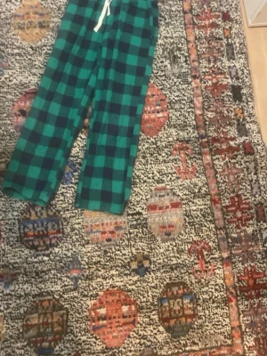 Gröna rutiga pyjamasbyxor - Mysiga pyjamasbyxor i grönt och mörkblått rutmönster med vit dragsko i midjan. Perfekta för chillkvällar hemma. Byxorna har rak passform och är tillverkade i mjukt tyg för extra komfort.