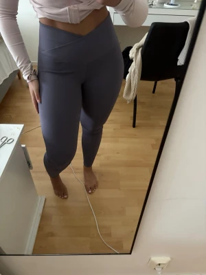 Träningstights med V-formad midja - Säljer ett par lila leggings med hög midja och snygg V-formad linning. De är tighta och stretchiga, perfekta för träning eller chill. Materialet känns mjukt och följsamt mot kroppen. Helt felfria!