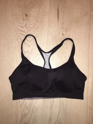 Svart sport-bh Champion - Svart sport-bh från Champion med brottarrygg. Medium support. Snygg och enkel design med elastisk kant nedtill och liten logga på ryggen. Storlek 34 C. Passar xs. 