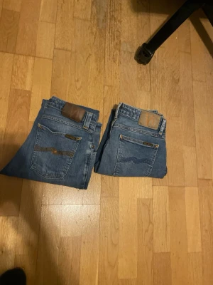 Blå slim jeans från Nudie Jeans 2x - Säljer ett par klassiska blå jeans från Nudie Jeans med slim passform. Jeansen har snygga detaljer på bakfickorna och är tillverkade i bomull. Perfekta för dig som gillar en enkel men stilren look.