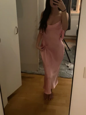 Rosa långklänning med öppen rygg - Säljer en elegant rosa långklänning i satinliknande material. Klänningen har smala axelband, figurnära passform och en snygg öppen rygg med cut out-detalj. Perfekt för dig som vill sticka ut med en feminin och stilren look.