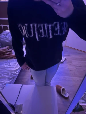 Svart tröja med vit text - Cool svart tröja med vit text över bröstet i en lite sliten stil. Tröjan har en klassisk passform med långa ärmar och rund hals. Perfekt för en avslappnad och trendig look.