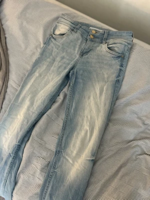 Ljusblå skinny jeans från Bershka - Säljer ett par ljusblå utsvängda jeans från Bershka med snygg slitning och klassisk femficksmodell. Gylf med dragkedja och två silverfärgade knappar. Perfekta för en avslappnad och trendig look.PRIS KAN DISKUTERAS 
