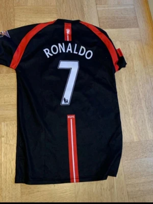 Ronaldo tröja  - Säljer en svart Manchester United fotbollströja från Nike med röda detaljer, AIG sponsortryck och klubbmärke fram. På ryggen står det Ronaldo och nummer 7. Tröjan har korta ärmar och är tillverkad i funktionsmaterial.