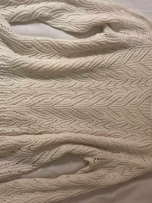 Vit stickad tröja med mönster - Snygg vit stickad tröja med unikt vågigt hålmönster på ärmar och framsida. Tröjan har rund halsringning och är tillverkad i ett mjukt garn som känns skönt mot huden. Perfekt för lager-på-lager och ger en stilren look.