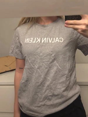 Grå Calvin Klein t-shirt - Snygg grå t-shirt från Calvin Klein med klassisk logga tryckt i vitt över bröstet. T-shirten har rund halsringning och korta ärmar. Perfekt basplagg som funkar till allt och är tillverkad i mjuk bomull.