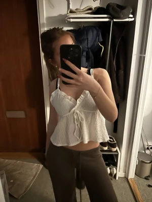 Vit omlott linnetopp med knyt - Söt vit linnetopp med omlottdesign och knyt framtill. Toppen är ärmlös med smala axelband och har en lätt volang nertill. Perfekt för varma dagar och enkel att styla till olika outfits.