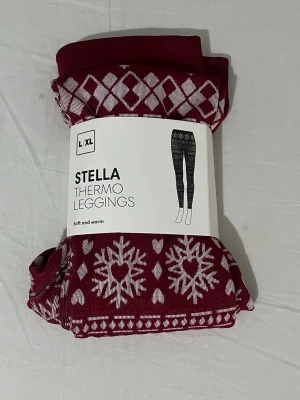 Vinröda Stella thermo leggings - Mysiga vinröda thermo leggings från Stella med vitt vintermönster av snöflingor och hjärtan. Leggingsen är mjuka, stretchiga och perfekta för kalla dagar. Materialet är varmt och bekvämt, och midjan är hög för extra komfort.