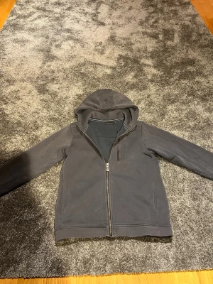 Mörkgrå Sail racing hoddie  - Snygg mörkgrå hoodie från Blend med dragkedja framtill och huva. Hoodien har en diskret broderad logga på huvan, två sidofickor och en bröstficka med dragkedja. Tillverkad i mjukt bomullsmaterial som är skönt mot huden. Perfekt för en avslappnad streetwear-look.