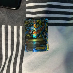 Pokémonkort M Charizard EX - Säljer ett Pokémonkort av typen M Charizard EX med 230 HP. Kortet har en färgstark och glansig design med blå, gul och svart bakgrund samt holografiska effekter. Perfekt för samlare eller Pokémonfans som vill utöka sin kortsamling. Kortet är värt runt 3000 