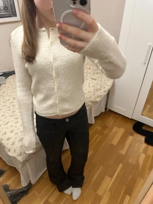 Vit kofta med knappar - Mysig vit kofta med fluffig textur och långa ärmar. Koftan har rund halsringning och stängs med små vita knappar framtill. Passar perfekt till jeans eller kjol för en enkel och stilren look.