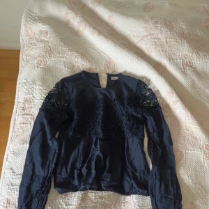 Mörkblå blus med spets från Abercrombie - Supersnygg mörkblå blus från Abercrombie & Fitch i storlek XS. Blusen har långa ärmar och v-ringning, samt vackra spetsdetaljer över bröstet och axlarna. Perfekt för dig som gillar en romantisk och trendig stil.