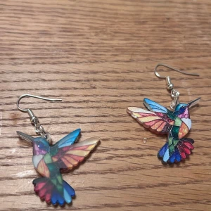 Färgglada kolibri örhängen - Unika örhängen i form av kolibrier med färgglada detaljer i blått, rosa, grönt, rött och gult. Lätta och iögonfallande med silvriga krokar. Perfekta för dig som vill sticka ut med ett lekfullt och konstnärligt smycke.