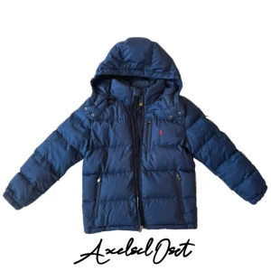 Mörkblå dunjacka Polo Ralph Lauren - Mörkblå dunjacka från Polo Ralph Lauren med huva, dragkedjor och klassisk röd logga på bröstet. Jackan har quiltad design, flera fickor med dragkedja och snygga detaljer i metall. Perfekt för kalla dagar och riktigt stilren look. Obs går ej att stänga. Trasig dragkedja därav billigt pris 