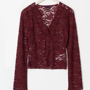 Vinröd spetsblus från Gina Tricot - Säljer en vinröd långärmad blus från Gina Tricot i genombruten spets med blommigt mönster. Toppen har v-ringning och är figurnära med snygga detaljer i spetsen. Perfekt för dig som vill sticka ut med en trendig och feminin look.