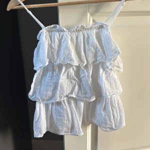 Vit volangig linnetopp från Gina Tricot - Supersöt vit linnetopp från Gina Tricot med flera lager volanger och tunna axelband. Toppen har en luftig känsla och är perfekt för varma dagar. Tillverkad i ett lätt bomullsmaterial som känns skönt mot huden. Har oftast storlek S/M så den passar även mig. Eftersom storleken är liten 