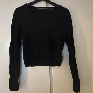 Svart ribbad tröja från The Black Label - Svart ribbad tröja från The Black Label Collection i storlek XS. Tröjan har v-ringning, lång ärm och är figurnära i modellen. Perfekt att styla med jeans eller kjol för en clean look. Toppen som höstplagg!