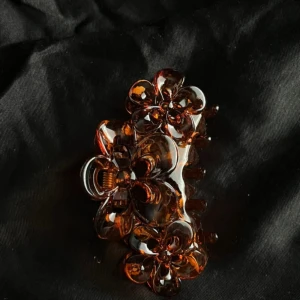 Brun blommig hårklämma - Snygg hårklämma i transparent brun plast med blommiga detaljer. Perfekt för att sätta upp håret på ett trendigt sätt. Klämman har en cool form med flera blommor och ger en extra touch till din look.