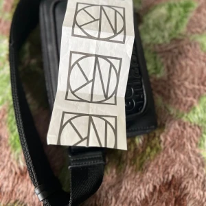 Svart axelväska från Hugo - Snygg svart axelväska från Hugo med präglad logotyp på framsidan och justerbart band. Väskan har två dragkedjefack och är gjord i syntetmaterial. Perfekt för att bära det viktigaste och ge din outfit en clean vibe.