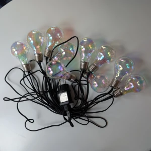 Dekorationsslinga med LED-glödlampor - Färgglad dekorationsslinga med 10 LED-glödlampor, ansluts till vägguttag. Ger ett vackert sken med regnbågseffekt, perfekt för fest eller mysbelysning. Svart kabel, EU-kontakt. Fint skick, inga synliga defekter eller slitage.