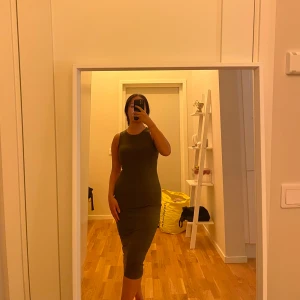 Olivgrön ärmlös midiklänning - Säljer en olivgrön, tight och ärmlös klänning med rund halsringning. Klänningen är midilång och har en enkel, stilren design som framhäver figuren. Perfekt för dig som gillar minimalistisk stil och vill ha något bekvämt men ändå snyggt.