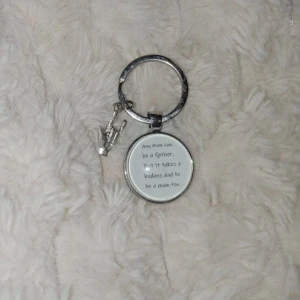 Nyckelring - Cool nyckelring i silverfärgad metall med rund bricka där det står 'Any man can be a father. But it takes a badass dad to be a mom too.' och en liten handberlock som gör rocktecknet. Perfekt accessoar till väskan eller nycklarna.