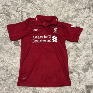 Liverpool M. Salah #11 fotbollströja - Liverpool FC matchtröja med M. Salah och nummer 11 på ryggen. Röd med vita tryck, klassisk krage och korta ärmar. Broderat klubbmärke, New Balance-logga och sponsorer som Standard Chartered och Western Union. Tillverkad i lätt polyester för bästa komfort. Size S eller XS. Ni får välja pris.