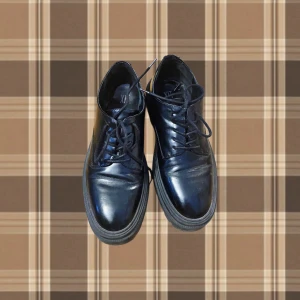 Svarta snörskor från XIT i skinn - Klassiska svarta snörskor från XIT i blankt skinn. Skorna har rund tå, platt sula och stilren design som passar till många olika outfits. Perfekta för dig som gillar en clean och tidlös look. Stor i storlek och hade också passat 41, har trasig sula men inget som syns på utsidan!