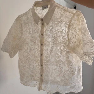 Beige spetsblus med blommigt mönster - Säljer en superfin beige spetsblus från Studio med blommigt broderat mönster och korta ärmar. Blusen är väldigt fin över klänning, till fest, jobbet eller till massa smycken! (Använd endast 2 gånger)
