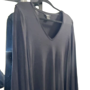 Svart tunika  med spets från Lindex - Svart långärmad tunika från Lindex med v-ringning och snygga spetsdetaljer vid ärmsluten. Tunikan har en enkel, rak passform och är tillverkad i ett mjukt material som känns skönt mot huden. Perfekt för dig som gillar stilrena plagg med en twist.