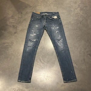 Dondup - Säljer ett par blå jeans med slimfit passform och slitna detaljer framtill. Jeansen har klassisk femficksdesign, dragkedja och knapp i midjan.