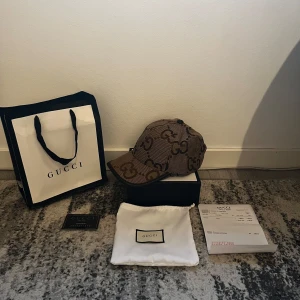 GG Keps Jumbo - Säljer en snygg beige keps. Kepsen har böjd skärm, justerbar rem bak i skinn och insida i ljusbeige bomull. Perfekt för dig som vill ha en lyxig och trendig accessoar med tydlig designerstil.